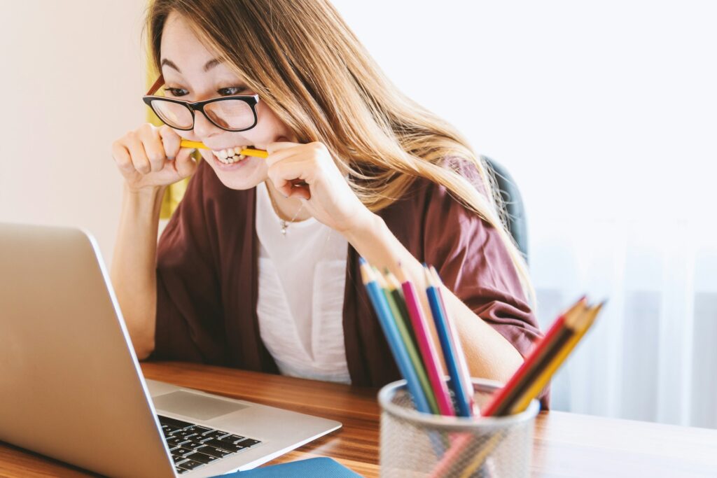 A girl biting pencil looking at laptop